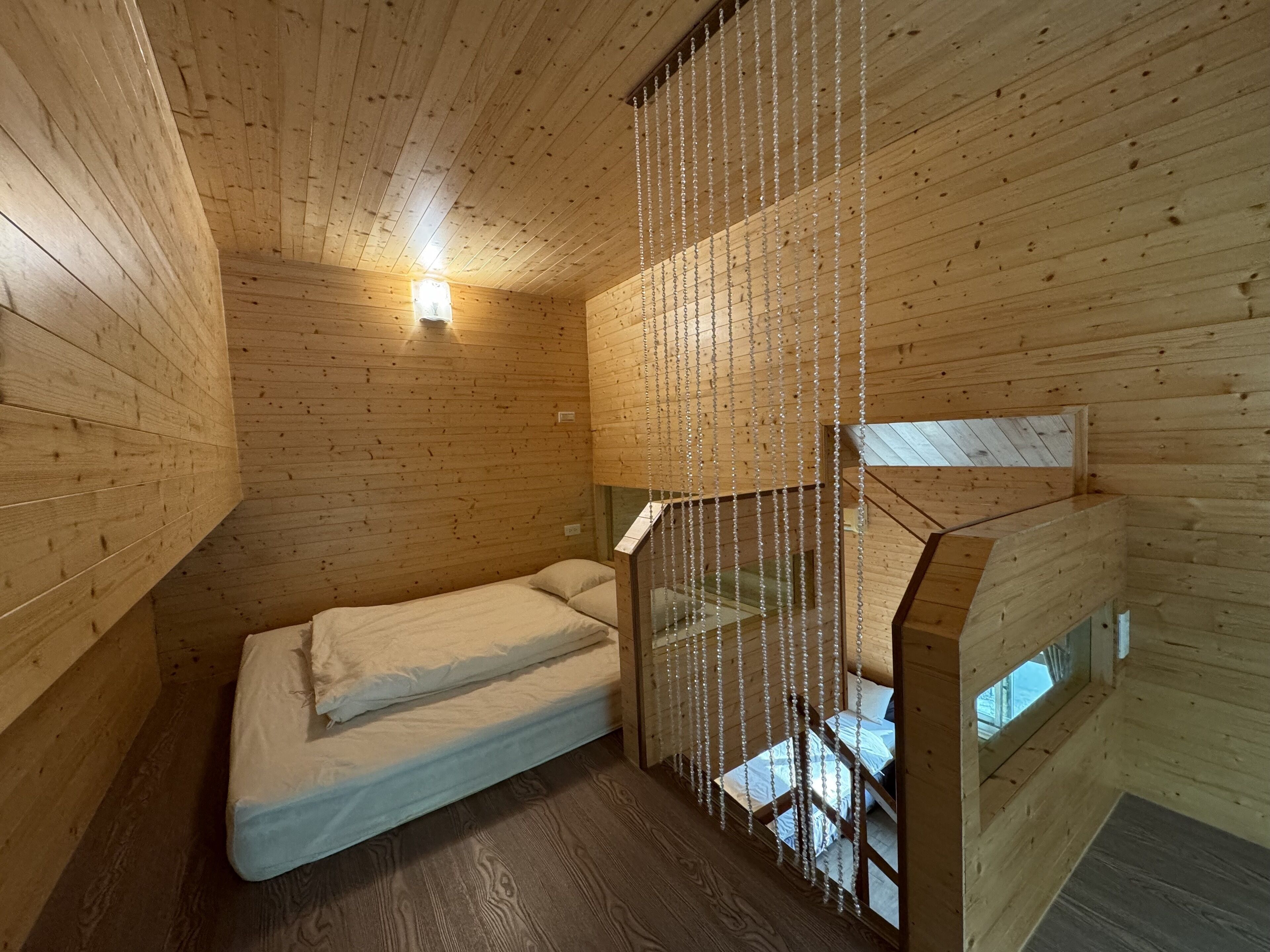 A small, wooden cabin room with a bed, a window, and a staircase.
