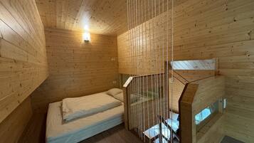 A small, wooden cabin room with a bed, a window, and a staircase.