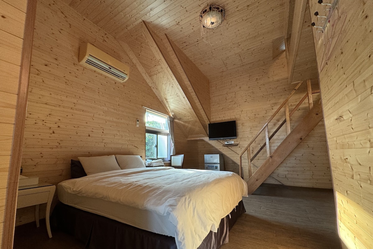 A wooden cabin bedroom with a bed, a desk, a chair, a television, and a staircase.