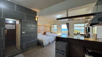 Una habitación de hotel moderna con una cama grande, una kitchenette compacta y vista al mar.