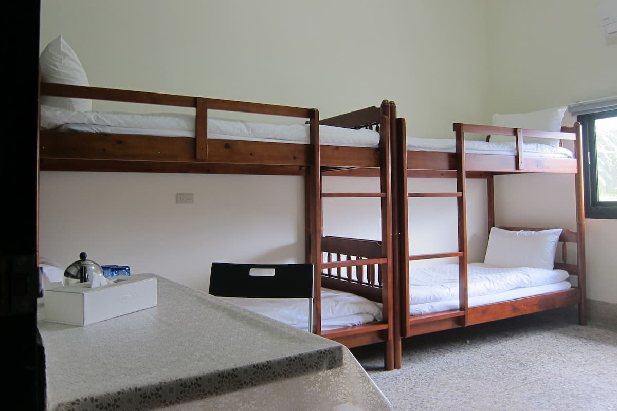 A bunk bed room with a desk and chair, a window, and a small table with a tissue box.