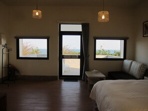 A hotel room with a bed, a small table, and two windows offering a view of the sea. - Runners' House Taitung (Changbin)