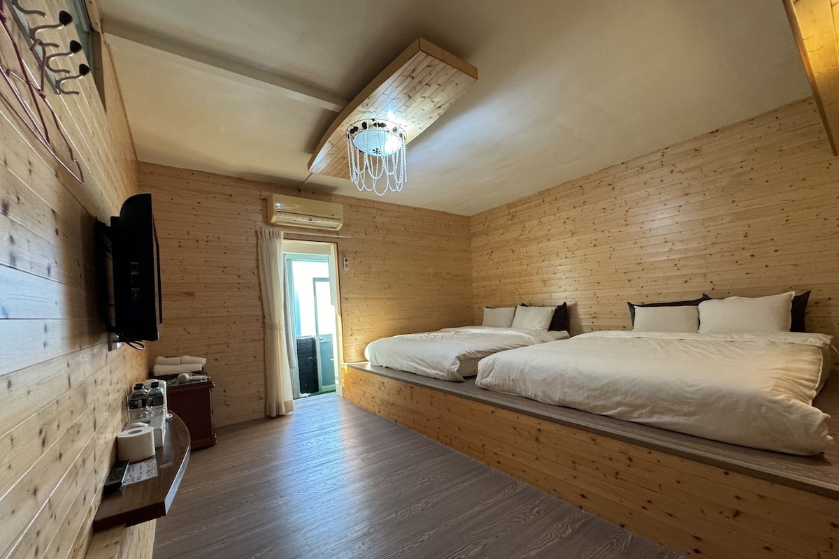 A wooden cabin room with two beds, a TV, a chandelier, and a wooden ceiling.