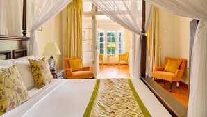 A hotel room with a bed, a nightstand, a lamp, two chairs, and a view of the garden through the open door. - Strathdon by Zinc Journeys (Ginigathena)