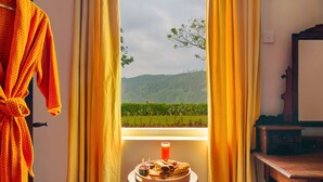 A room with a view of a vineyard through a window, a table with a plate of food, and a wooden dresser. - Strathdon by Zinc Journeys (Ginigathena)