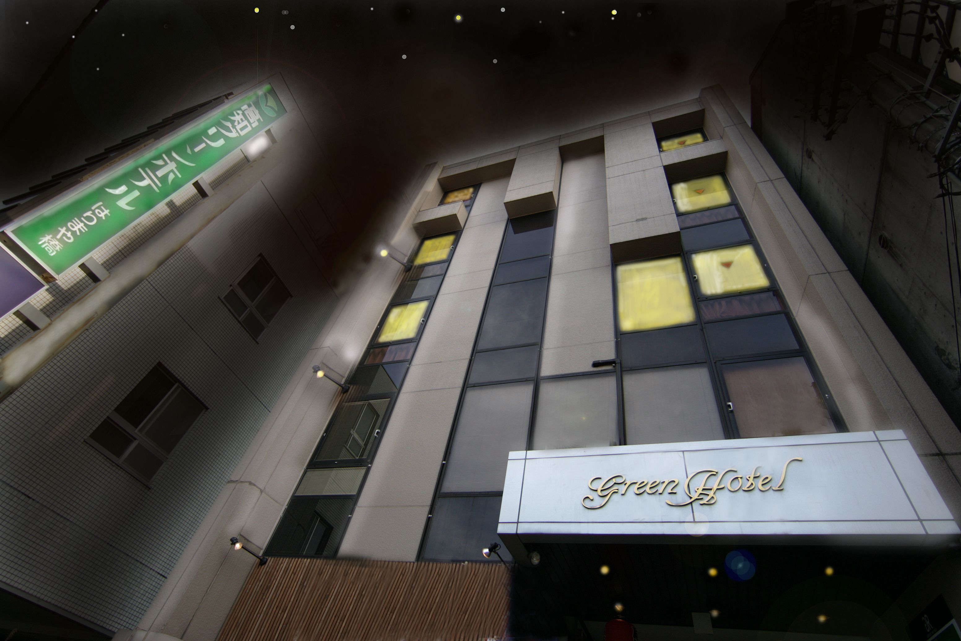 A hotel with a modern facade, large windows, and a prominent sign reading "Green Hotel".
