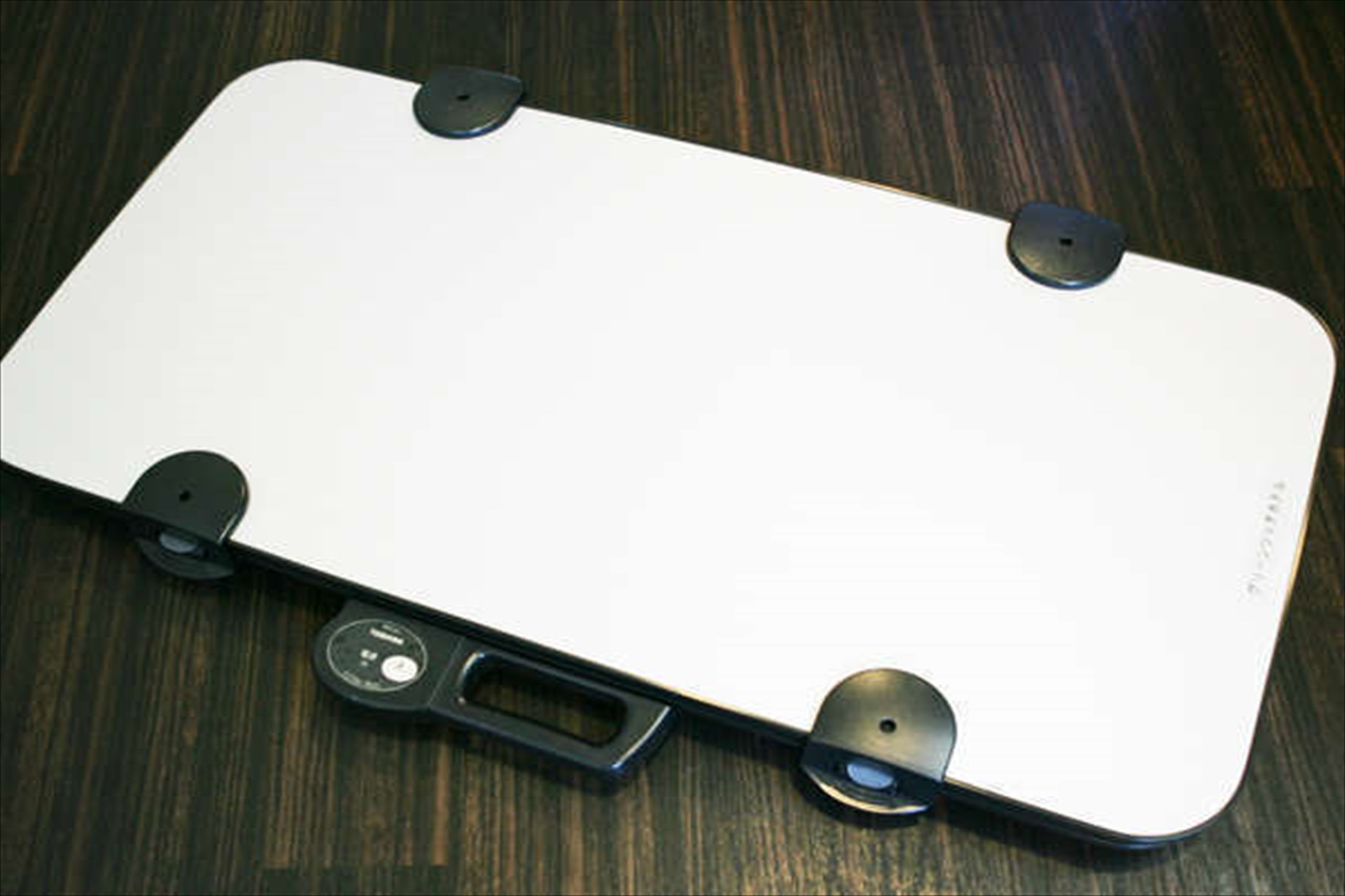 A white rectangular object with four circular indentations at the corners, a central rectangular cutout, and a small circular button on the front.