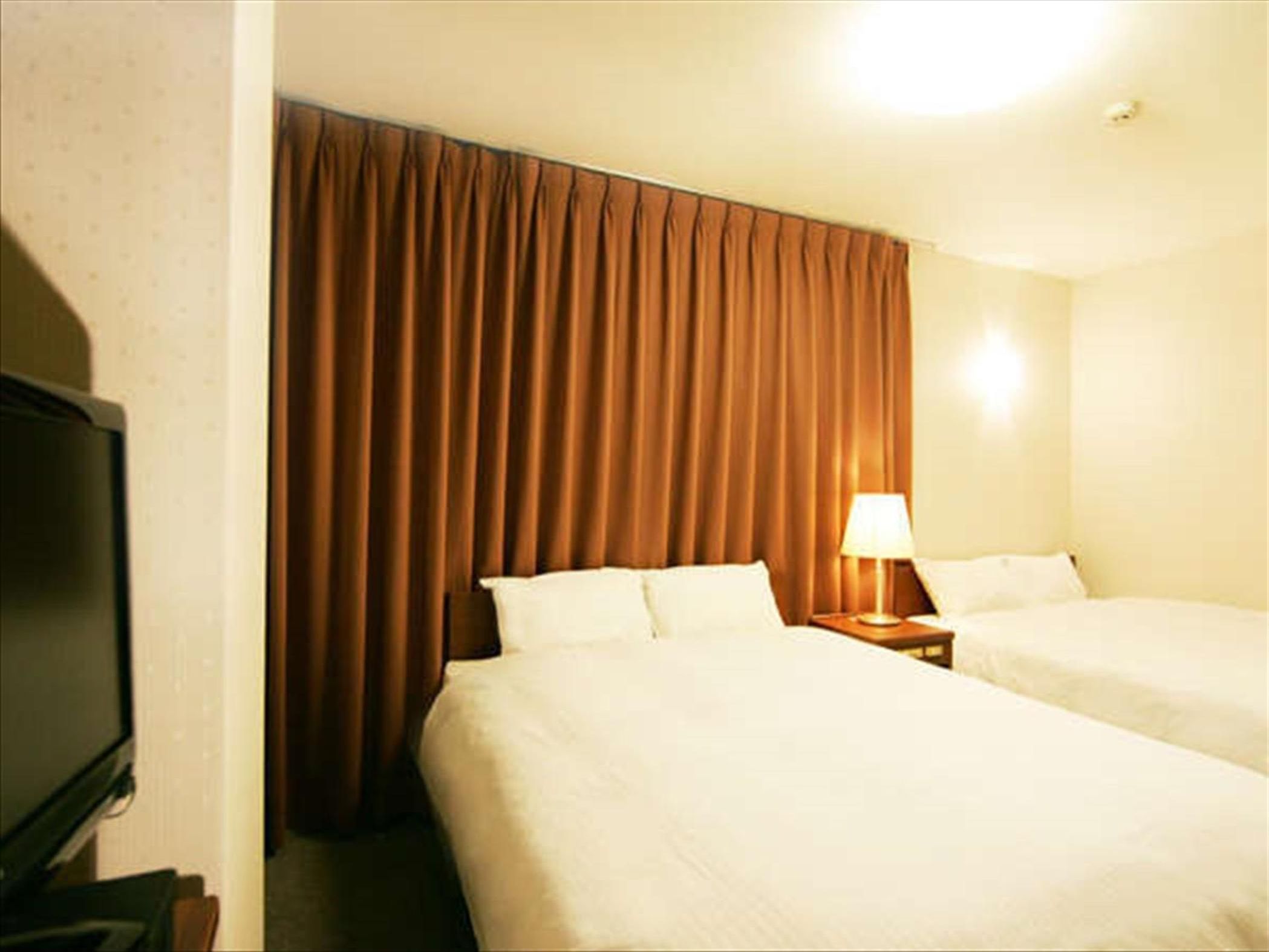 A hotel room with two beds, a nightstand with a lamp, and a television on the left.