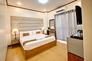 A hotel room with a large bed, bedside tables with lamps, a desk with a mirror, and a kitchenette. - Sur Beach Resort (Boracay Island)