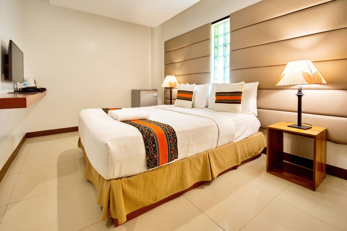 Une chambre d’hôtel avec un grand lit, deux tables de chevet, un téléviseur à écran plat et une fenêtre avec des stores.