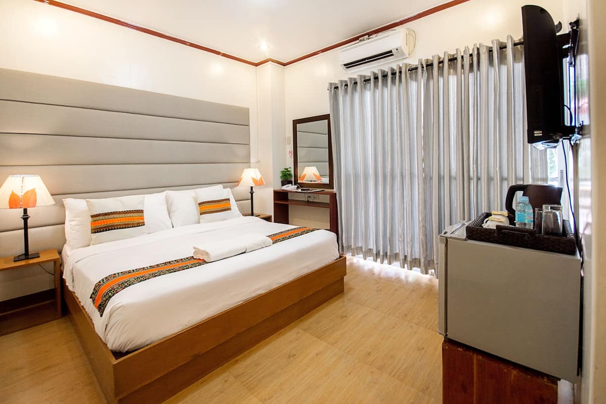 Une chambre d’hôtel avec un grand lit, des lampes de chevet, un bureau avec un miroir, un climatiseur et un réfrigérateur.