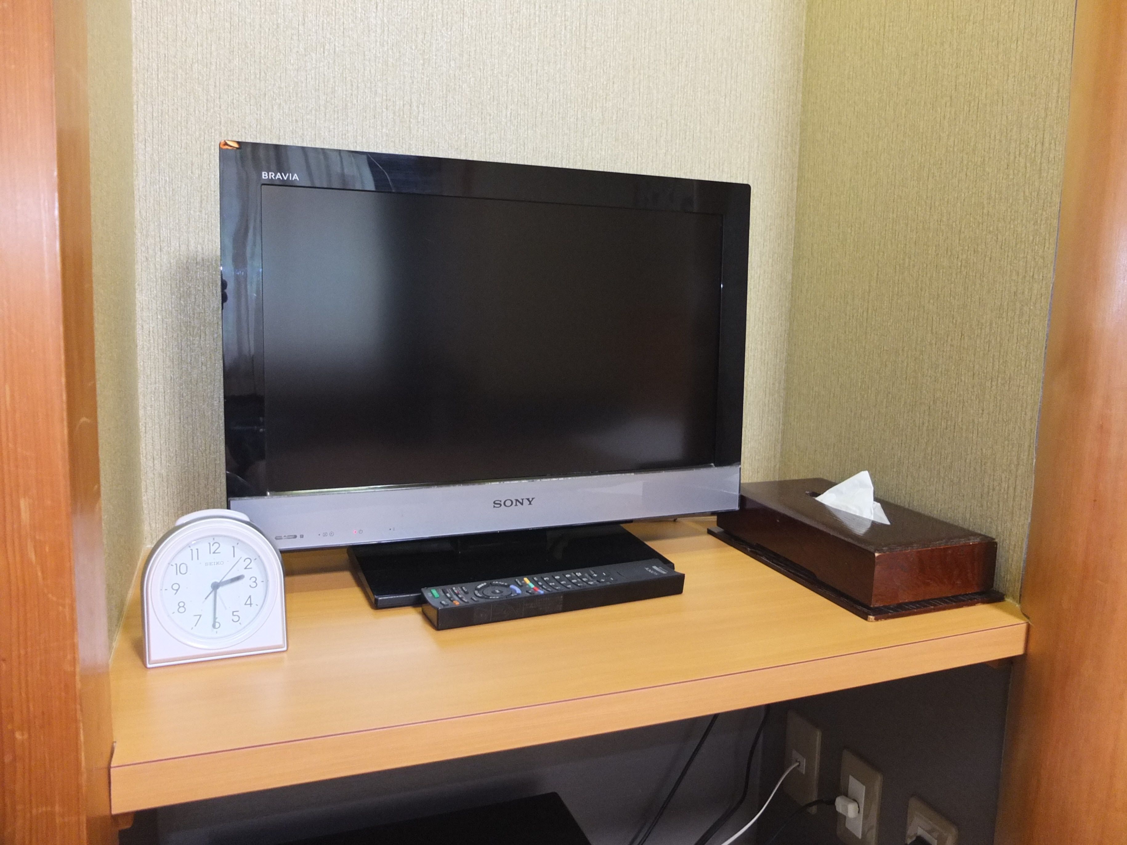 Un téléviseur à écran plat posé sur un meuble télé en bois, avec une télécommande et une horloge.