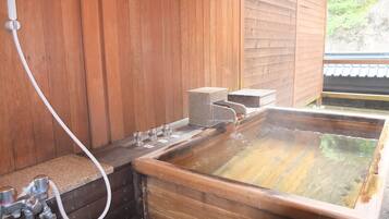 A wooden spa bath with a wooden floor, a stone bench, and a window with a view of greenery.