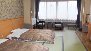 A hotel room with two beds, a small table, chairs, and a view of the outside through large windows.