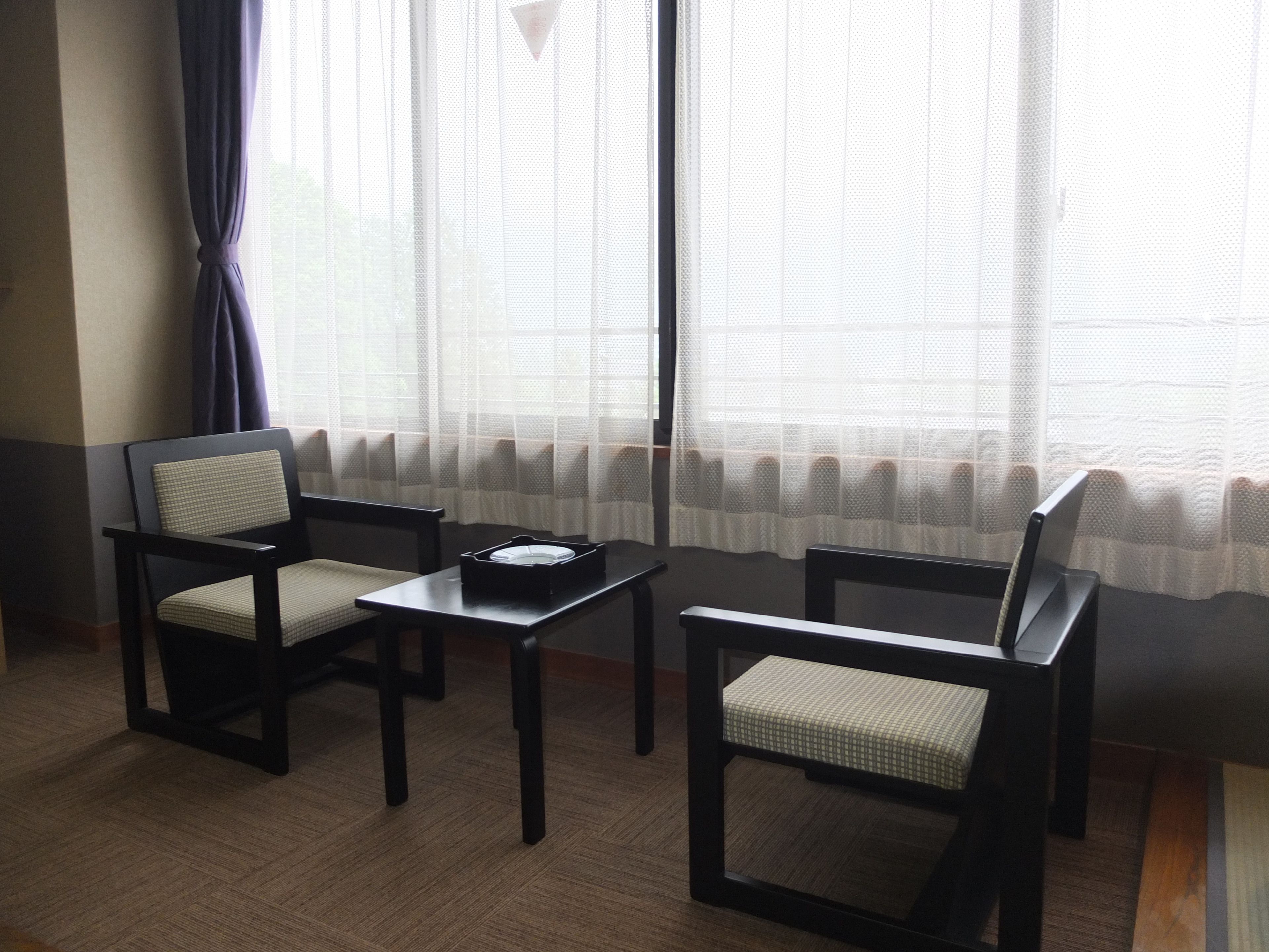 A room with two chairs, a small table, and a window with sheer curtains.