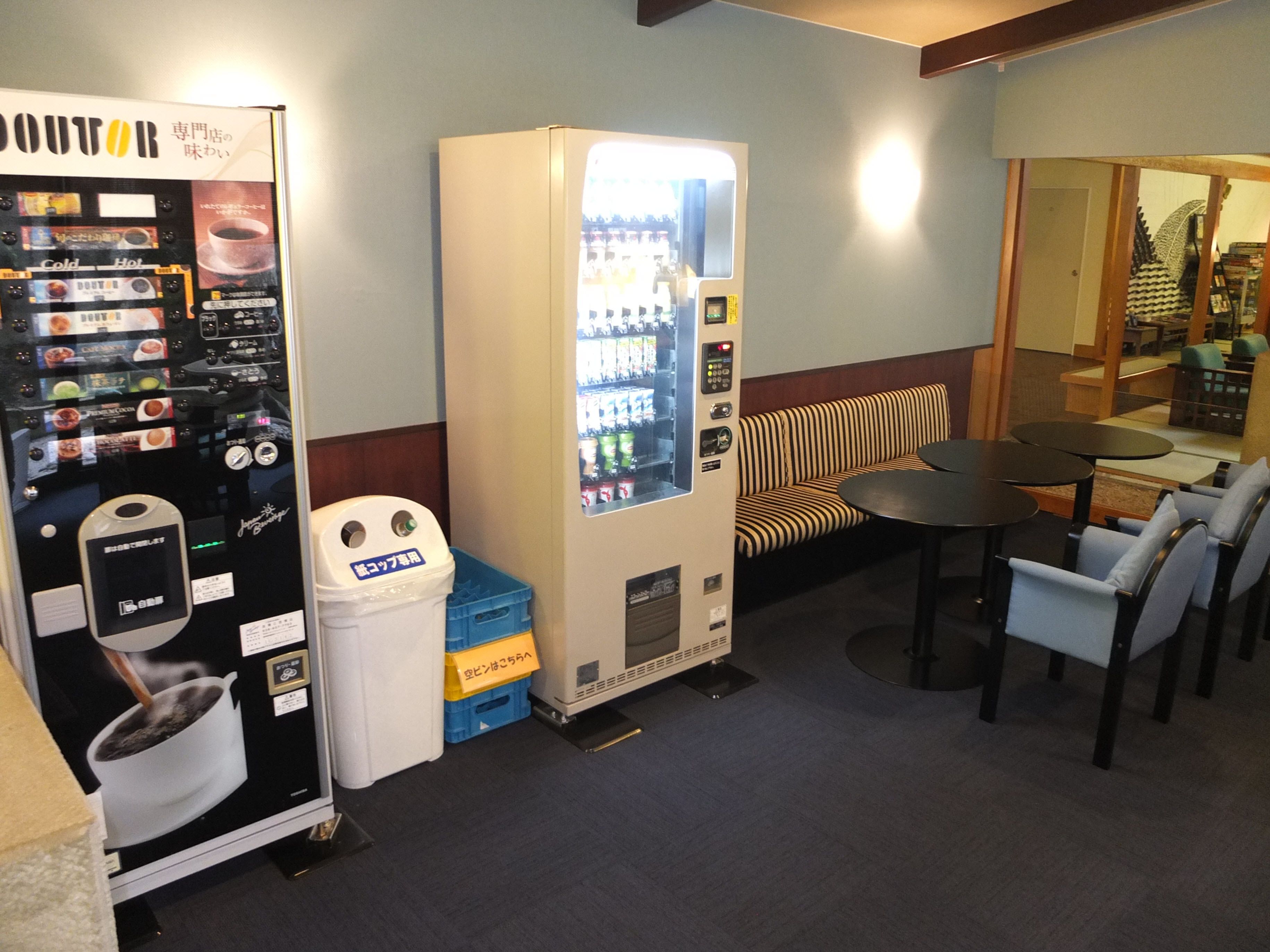 A vending machine and a trash bin in a room with a striped sofa and a table.
