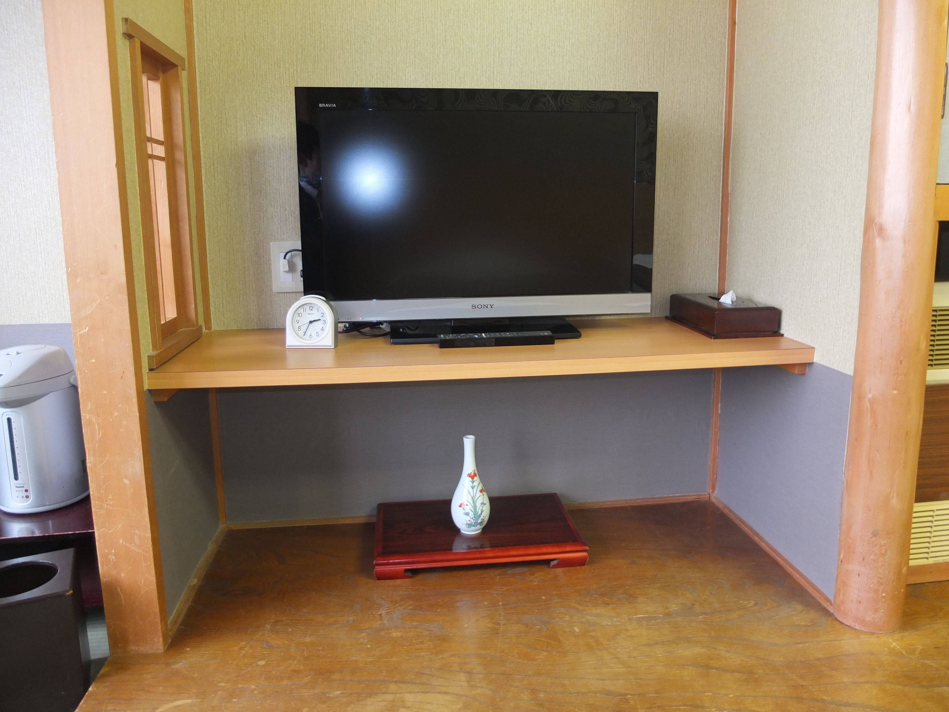 Een houten tv-meubel met een flatscreen televisie, een klok en een kleine vaas.