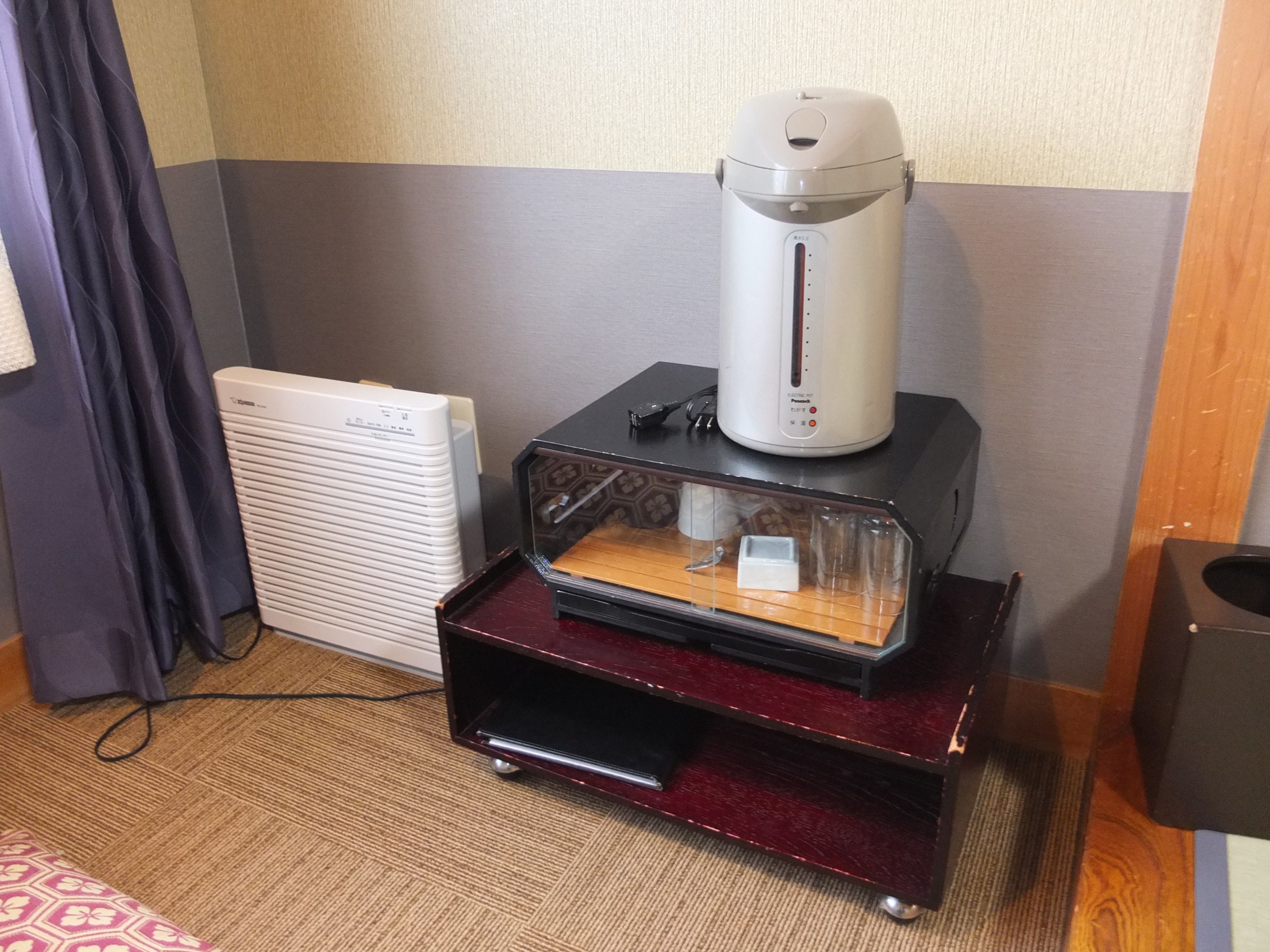 A room with a coffee maker on a wooden stand, a white radiator, and a patterned rug.