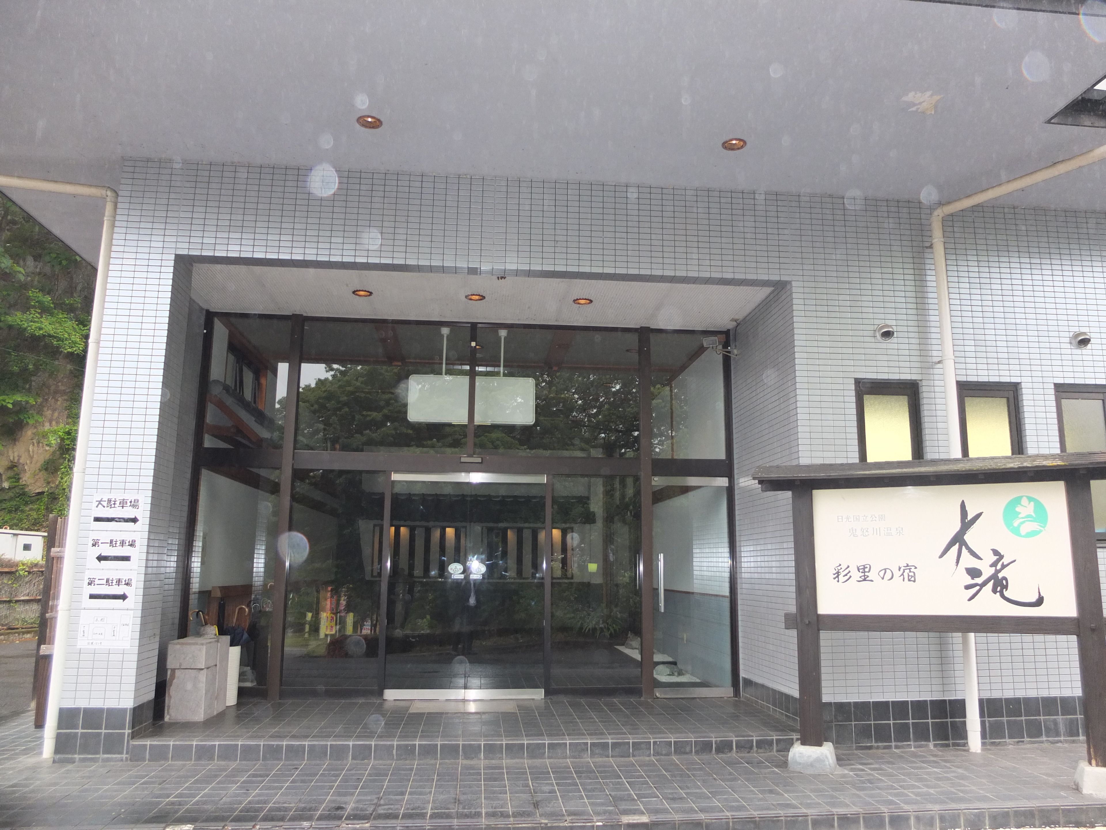 A building entrance with a tiled facade, glass doors, and signage indicating parking directions.