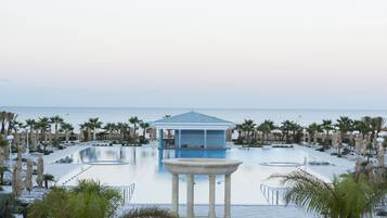 A pool area with a central structure, palm trees, and a view of the sea.