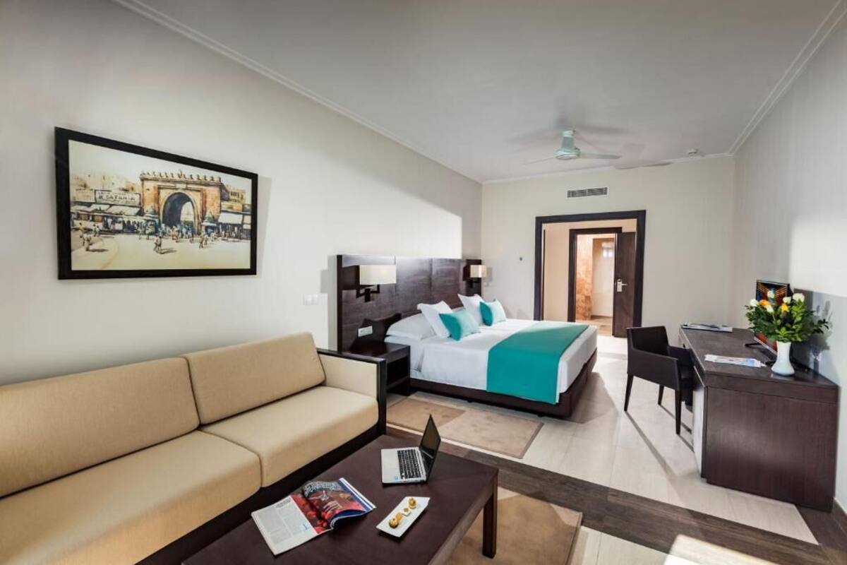 A hotel room with a bed, a sofa, a desk, and a laptop.