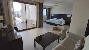 A hotel room with a balcony, a bed, a sofa, a coffee table, and a desk with a chair.