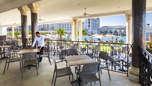 An outdoor patio with tables and chairs, overlooking a pool and buildings. - Hotel Concorde Green Park Palace (Port El Kantaoui)