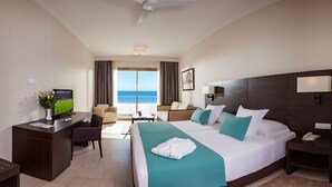 A hotel room with a large bed, a desk, a chair, a TV, a balcony with a view of the sea, and a ceiling fan. - Hotel Concorde Green Park Palace (Port El Kantaoui)