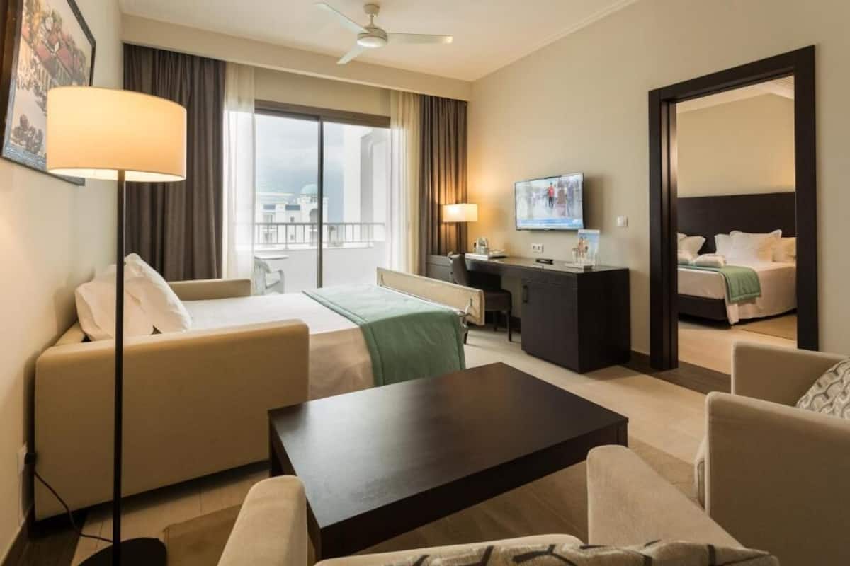 A hotel room with a bed, a sofa, a desk, a television, and a balcony with a view.