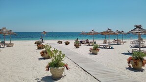 A beach with lounge chairs and thatched umbrellas, a wooden walkway, and potted plants. - Hotel Concorde Green Park Palace (Port El Kantaoui)