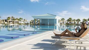 Un espace aménagé au bord de la piscine, avec des chaises longues, un coin salon abrité et des palmiers.