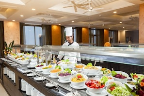 Un buffet proposant une variété de plats, un chef cuisinier et un intérieur moderne agrémenté d’un ventilateur de plafond.