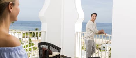 A balcony with wicker furniture, a view of the ocean, and a white railing.