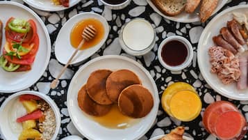 Una mesa de mármol con un desayuno abundante que incluye panqueques, huevos, tocino, tostadas y diversas frutas y bebidas.