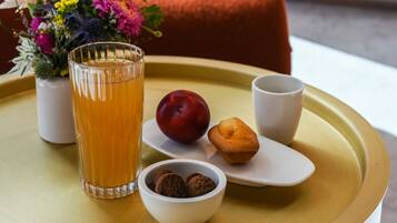 A tray with a glass of orange juice, a plum, a muffin, and a bowl of cookies on a round table.