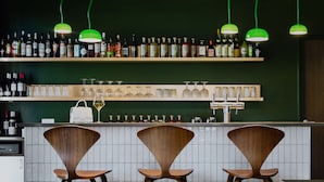 A bar area with three wooden chairs, a shelf of liquor bottles, and a row of wine glasses.