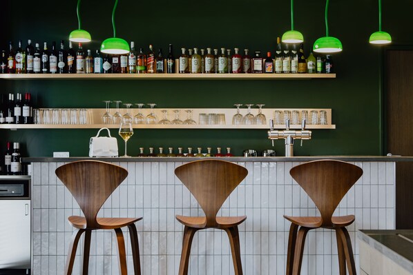 A bar area with three wooden chairs, a shelf of liquor bottles, and a row of wine glasses.