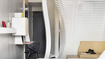 A modern hotel room with a bed, a desk, a chair, and a sofa.