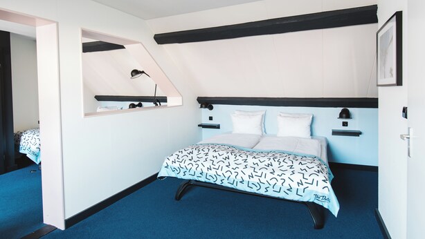 A bedroom with a bed, a bedside table, a mirror, and a shelf. - Hotel The Dutch (Maastricht)