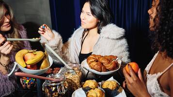 A group of people at a table with food and drinks, a blue curtain in the background, and a chandelier.
