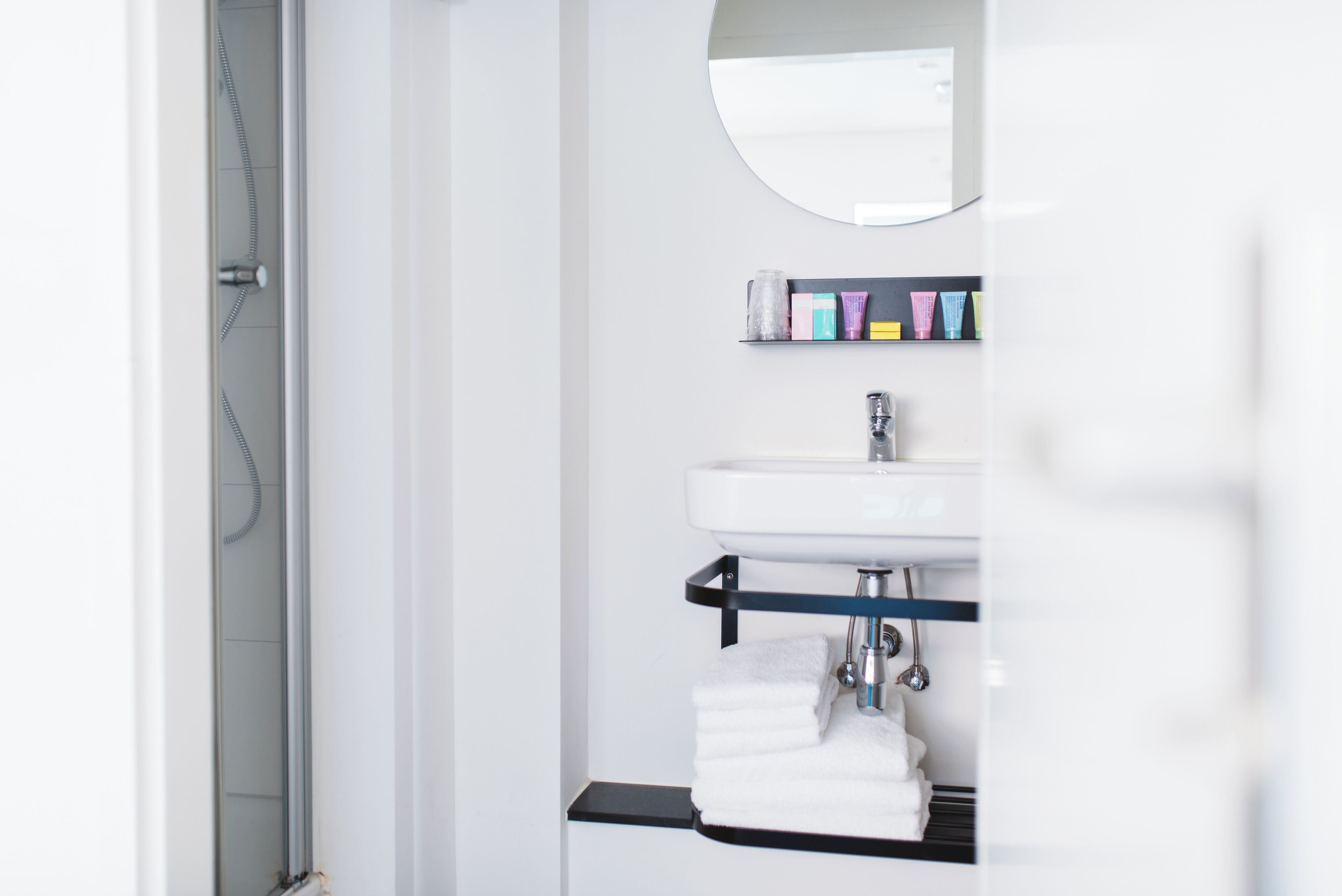 Une salle de bain avec un lavabo blanc, un miroir et une étagère contenant des articles de toilette.