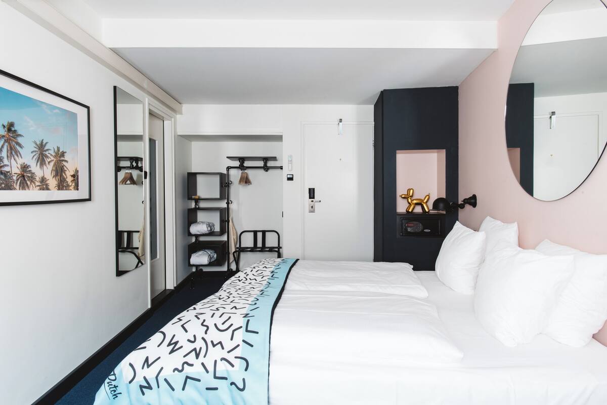 Ein Hotelzimmer mit einem Bett, einem großen Spiegel, einem Kleiderschrank und einer Tür zu einem weiteren Raum.