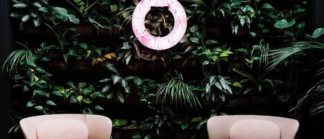 A room with two pink chairs, a round table, and a wall covered with green plants.