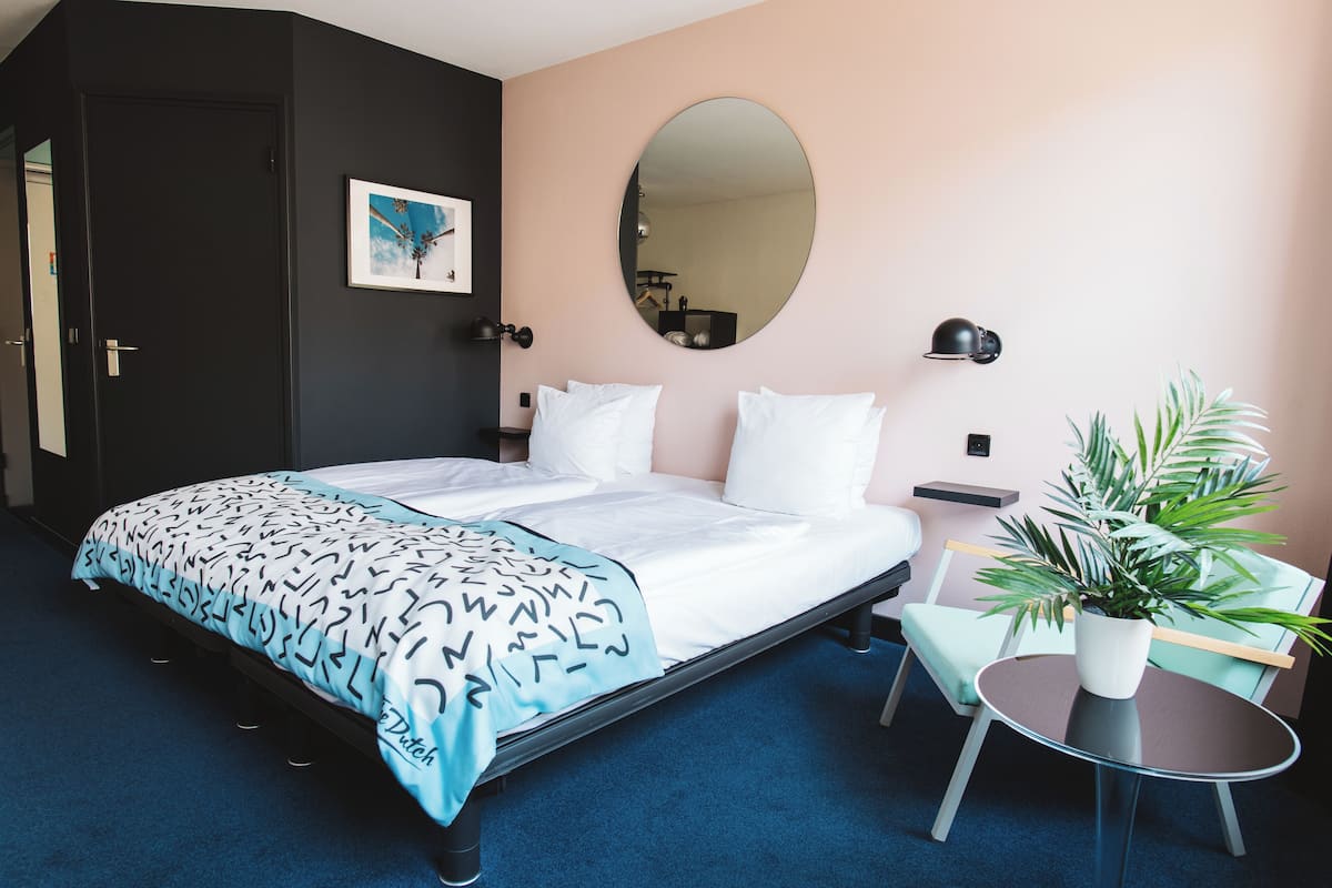 Ein ordentlich eingerichtetes Hotelzimmer mit einem Bett, Nachttischen, einem Spiegel, einem Sessel und einer Topfpflanze.