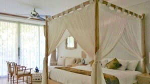 Ein Bett mit Baldachin, ein Holzkopfstück und ein Nachttisch mit Lampe. Es gibt eine Sitzecke mit Stühlen und einem kleinen Tisch.