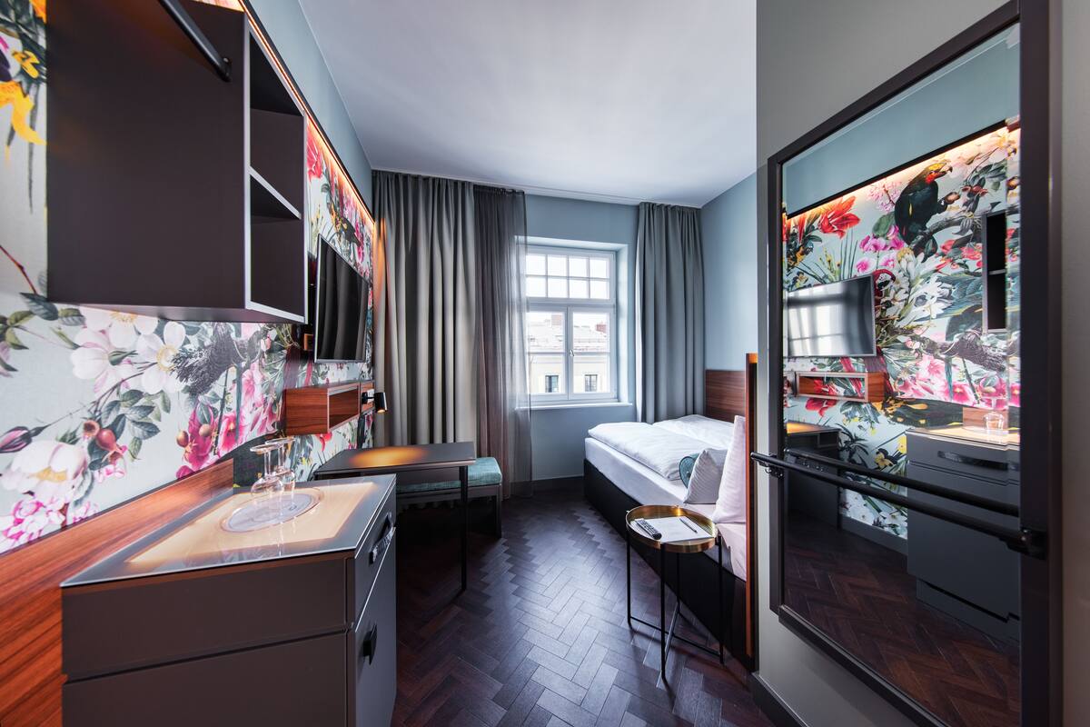 Habitación de hotel con cama, escritorio con computadora, una mesita con un vaso y una ventana con cortinas.