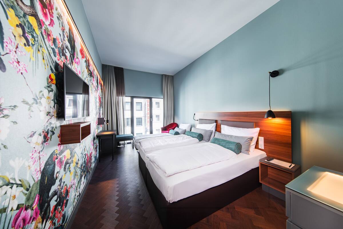 Una habitación de hotel con una cama grande, televisión, mesita de noche y ventana con cortinas.