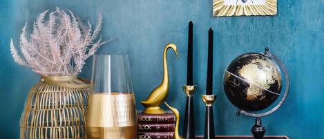 Una habitación con un globo terráqueo, libros, un florero con plantas secas, un candelabro y una cisne decorativo.