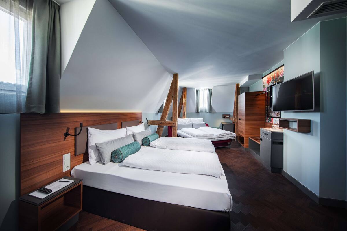 Una habitación de hotel moderna con una cama grande, un escritorio, un televisor y una zona de cocina.