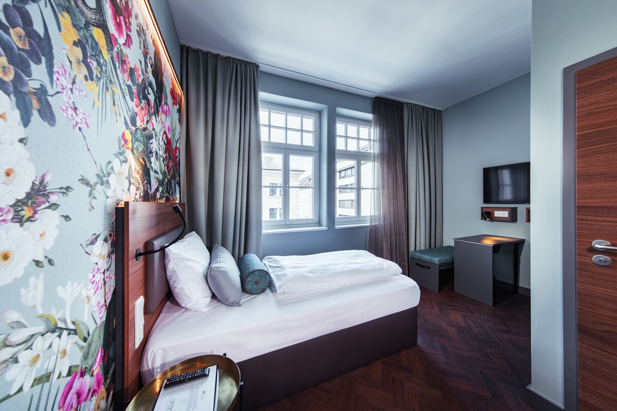 A hotel room with a bed, a desk, a television, and a window with curtains.